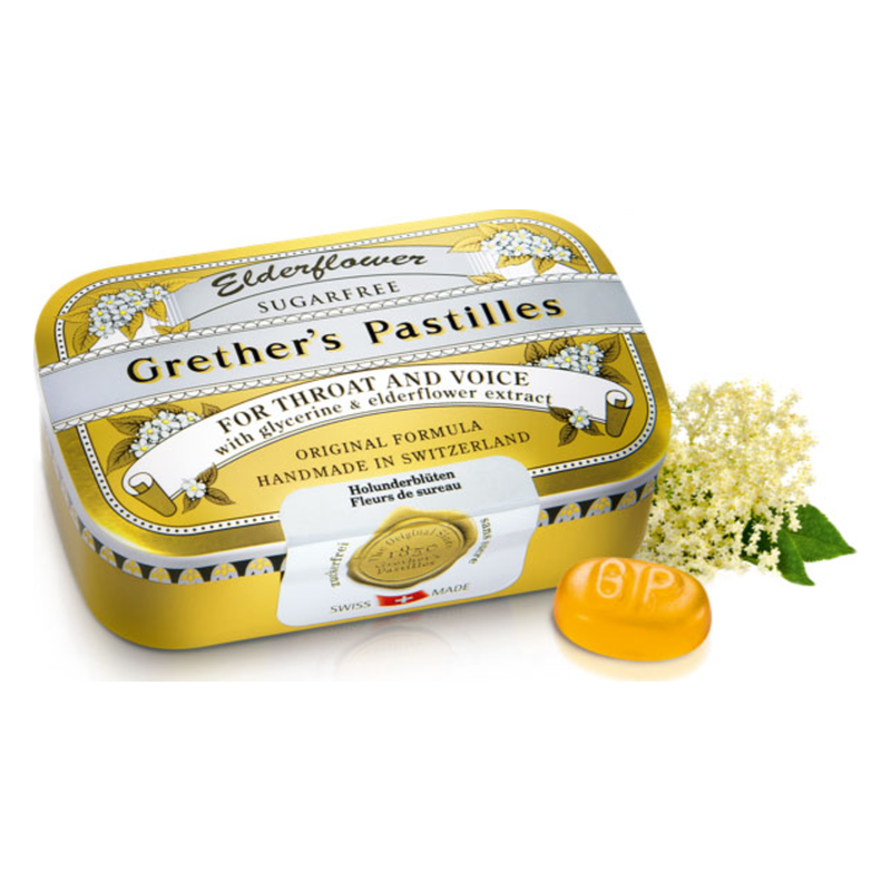 Gelbe Dose mit Grether's Pastillen für Hals und Stimme, umgeben von Holunderblüten.