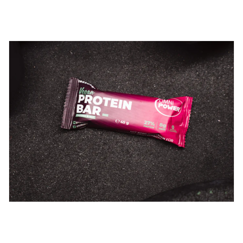 Eine vegane Proteinriegel-Verpackung in lila mit den Angaben zu Nährstoffen, auf dunklem Hintergrund.